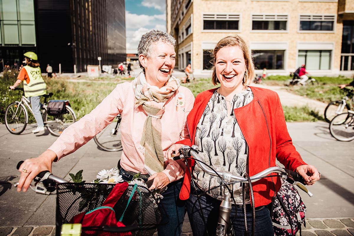 Twee fietsende vrouwen staan naast elkaar en lachen