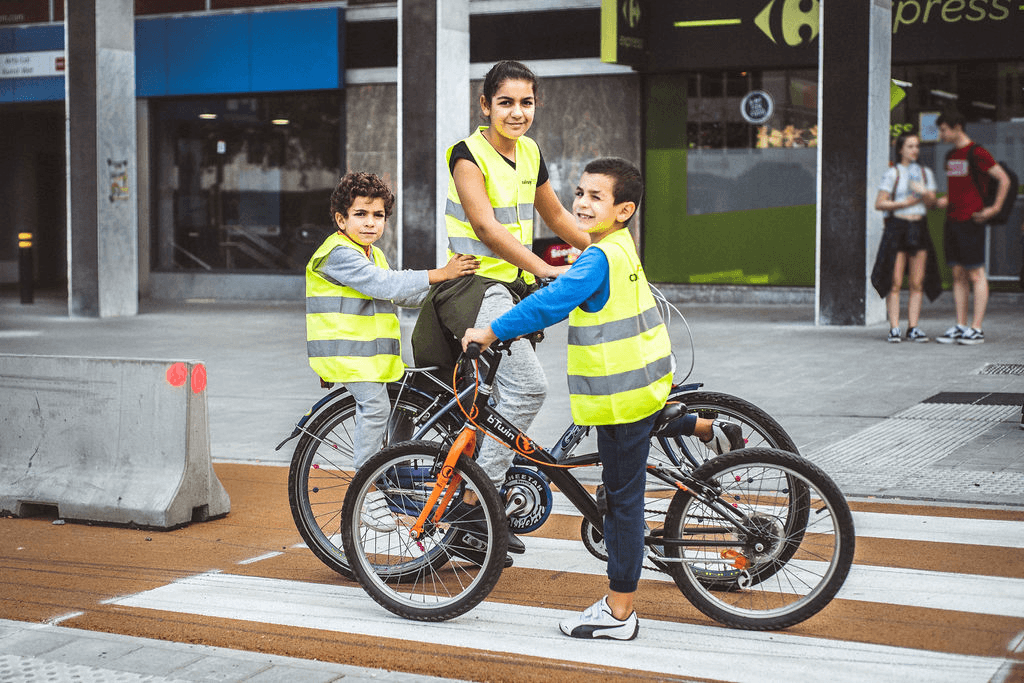 Drie kinderen staan met de fiets op het zebrapad en kijken naar de camera