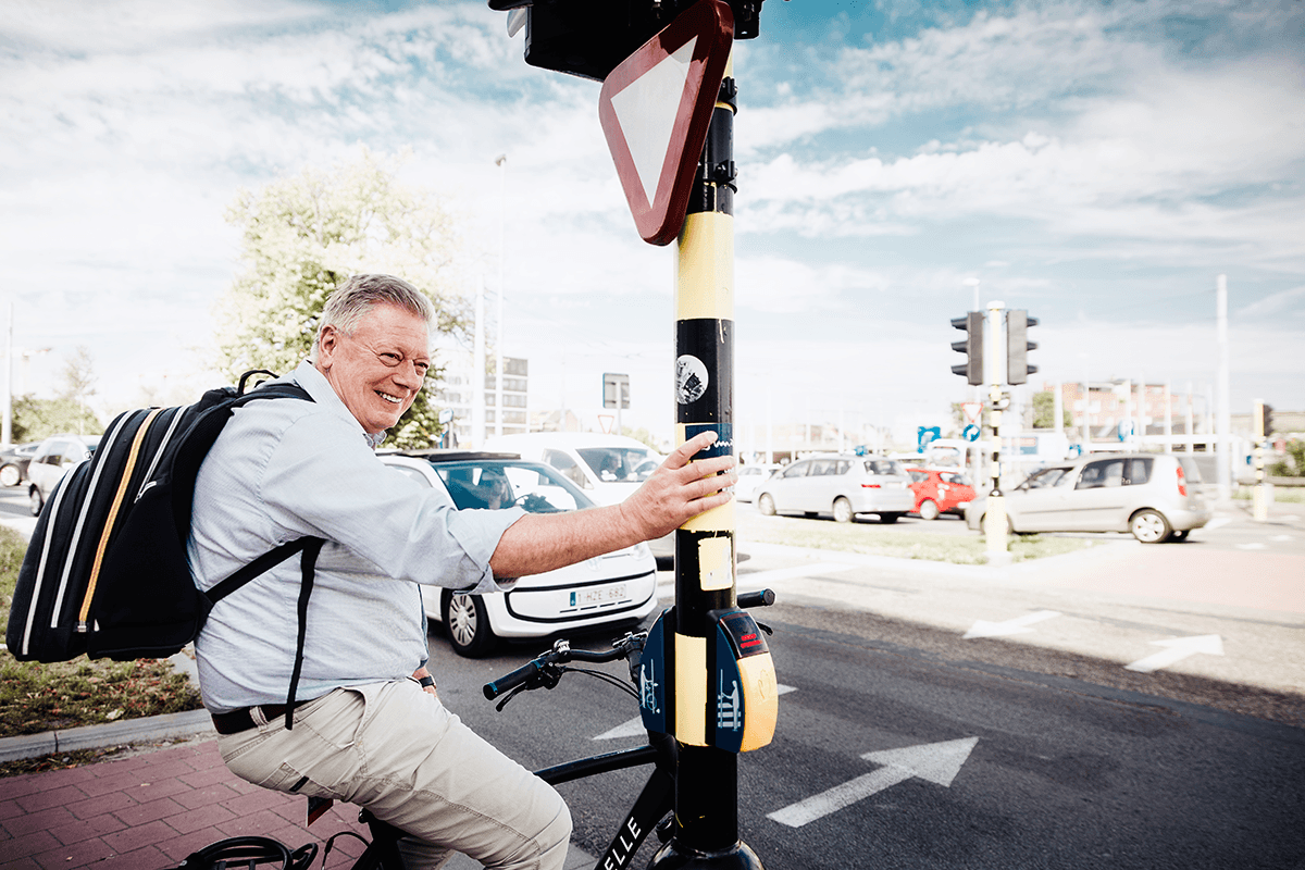 Man op fiets houdt zich in evenwicht aan een verkeerslicht terwijl hij wacht op groen
