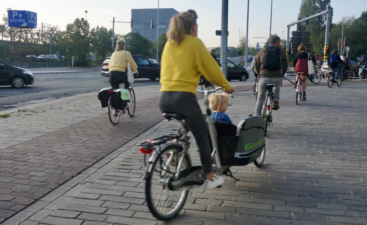  een witte vrouw met een paardenstaart en een kindje in een bakfiets, een vrouw met fietstassen, een man met een rugzak. Foto door Lieven Jacobs. 