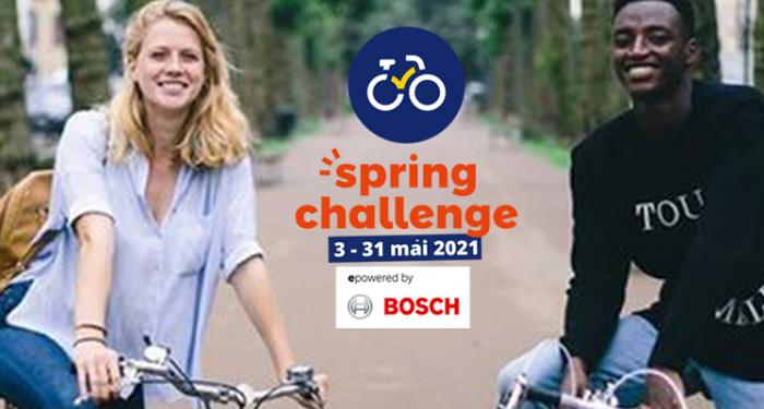 Twee fietsers staan op een fietspad waarlangs bomen staan. De vrouw links heeft een blauwe bloes en rood haar. De jongen rechts heeft een zwarte trui en is zwart. Ze lachen allebei naar de camera. 